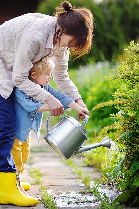 mujer ayudando a un niño a regar las plantas