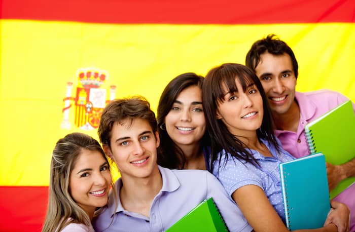 estudiantes con cuadernos en los brazos con la bandera española de fondo