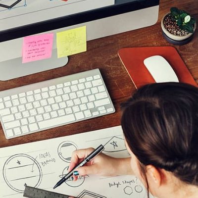 mujer diseñando logotipos en papel y en computadora